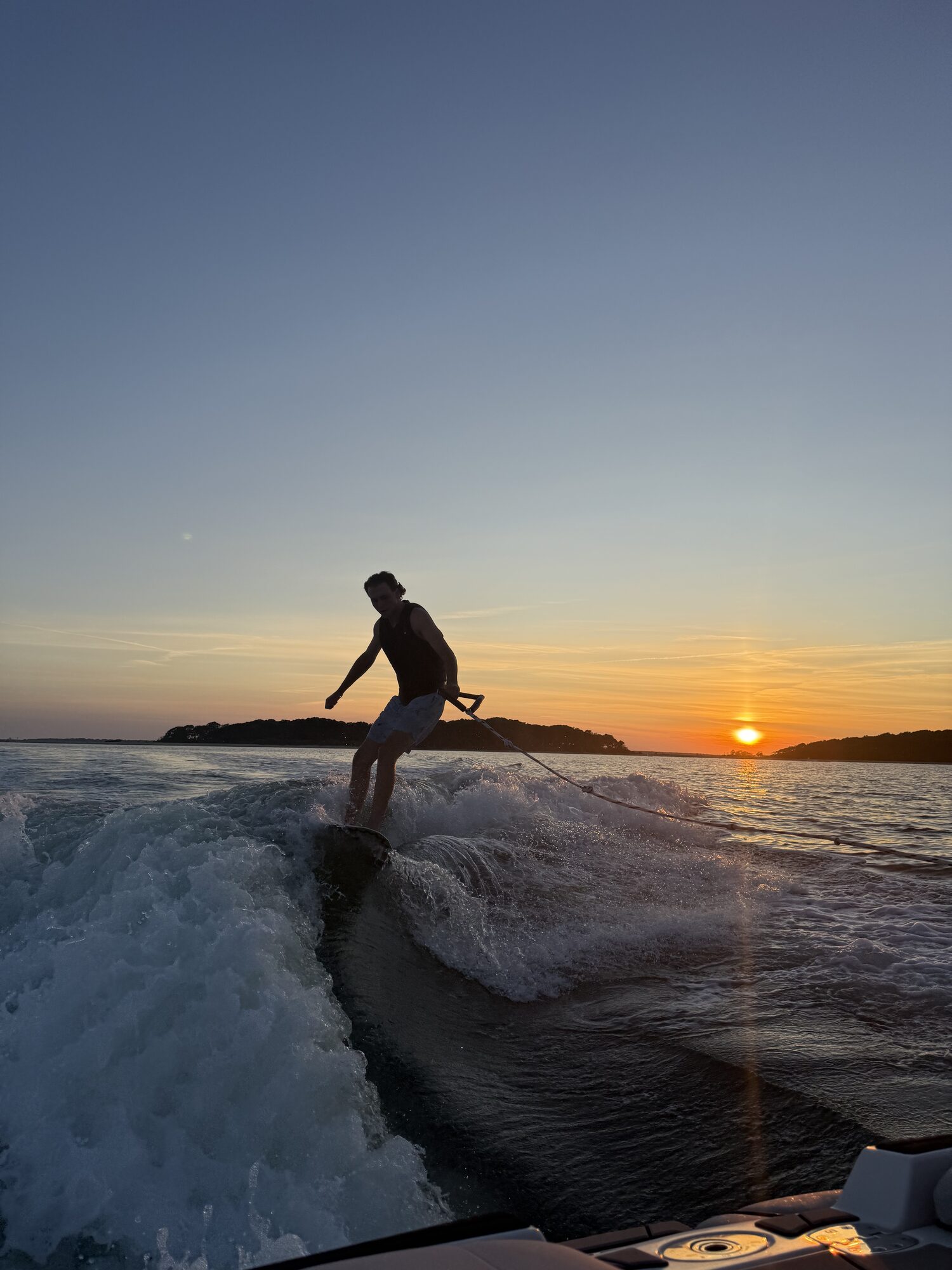 Wakesurfer silhouetted against the sunset behind a Hamptons charter